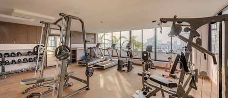 A modern gym with various exercise equipment, a weight rack, and a large window offering a city view.