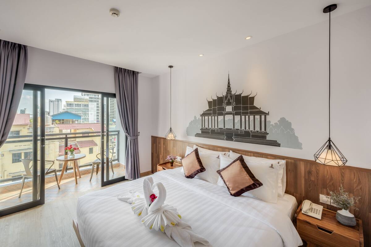 A hotel room with a large bed, a view of the city, a wall-mounted artwork, and a wooden headboard.