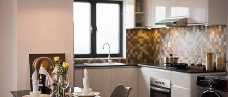 Una cocina moderna con comedor, que presenta una mesa negra, sillas blancas y una ventana con vistas.