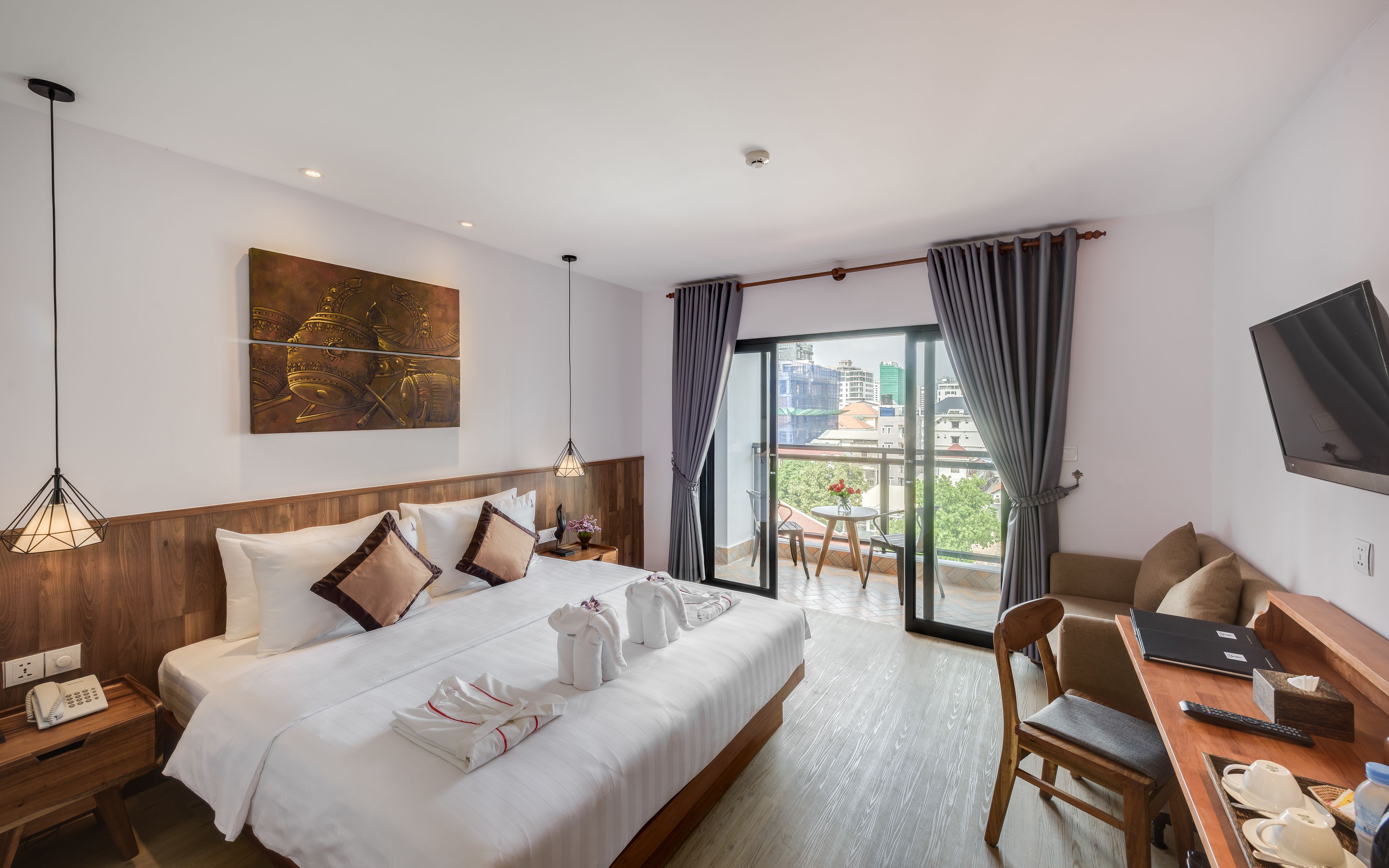 Habitación de hotel con cama, mesitas de noche, escritorio con silla, televisor y balcón con vistas a la ciudad.