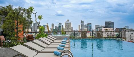 Una piscina en la azotea con sillones de descanso y un horizonte urbano de fondo.