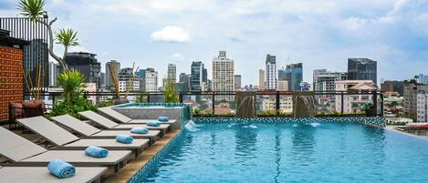 A rooftop infinity pool with lounge chairs and a city skyline view.