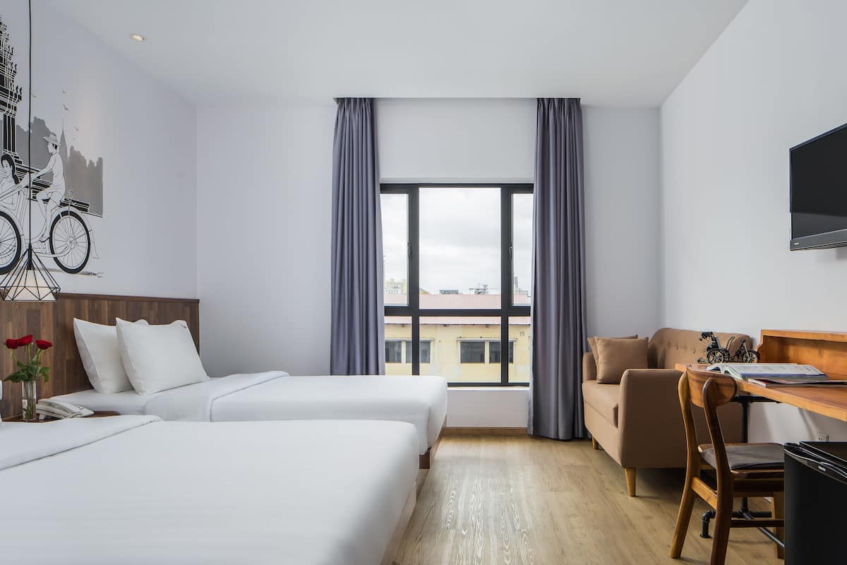 A hotel room with two beds, a desk, a chair, a TV, and a window with curtains.