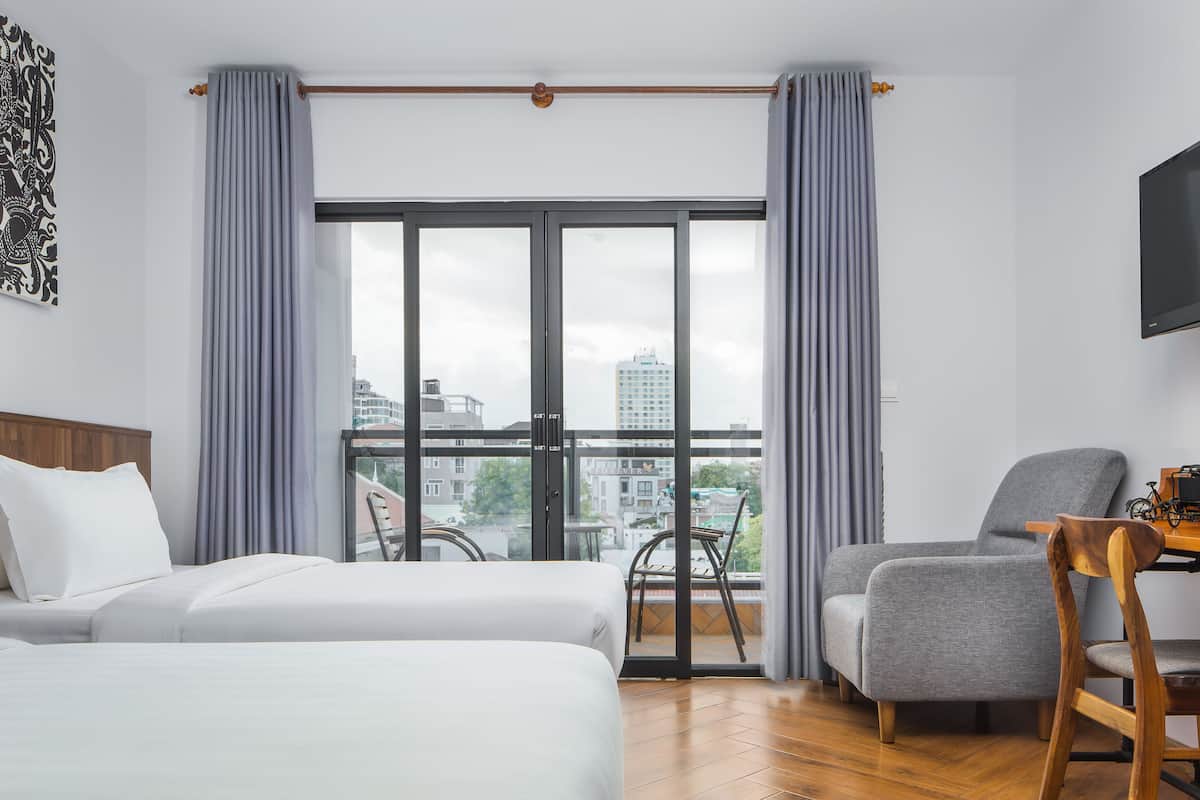 A hotel room with two beds, a balcony with a view of the city, a television, and a small table with a chair.