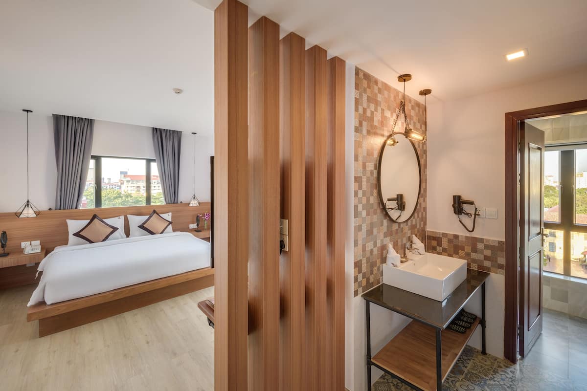 A hotel room with a bed, bedside table, and a bathroom with a sink and mirror.