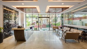A modern lobby with a marble reception desk, comfortable seating, large windows, and a view of the outside. - Phnom Penh 51 Hotel & Residences (Phnom Penh)