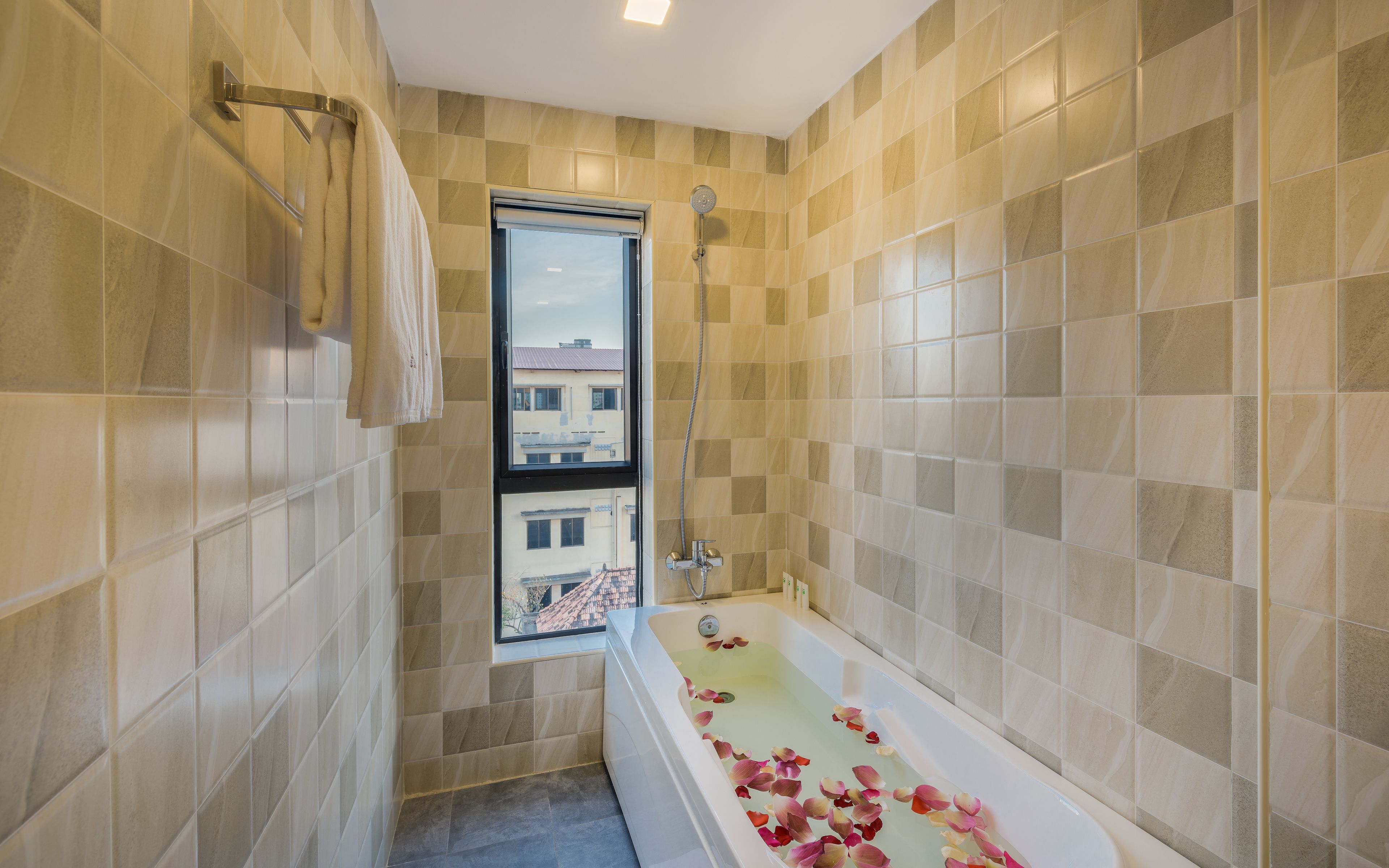 A bathroom with a bathtub filled with rose petals, a window, and a shower.