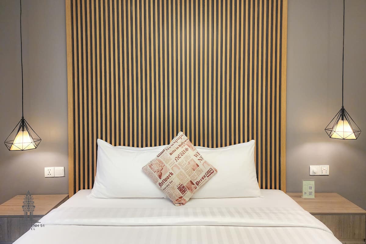 A neatly made bed with a pillow, a wooden slat headboard, and two pendant lights.