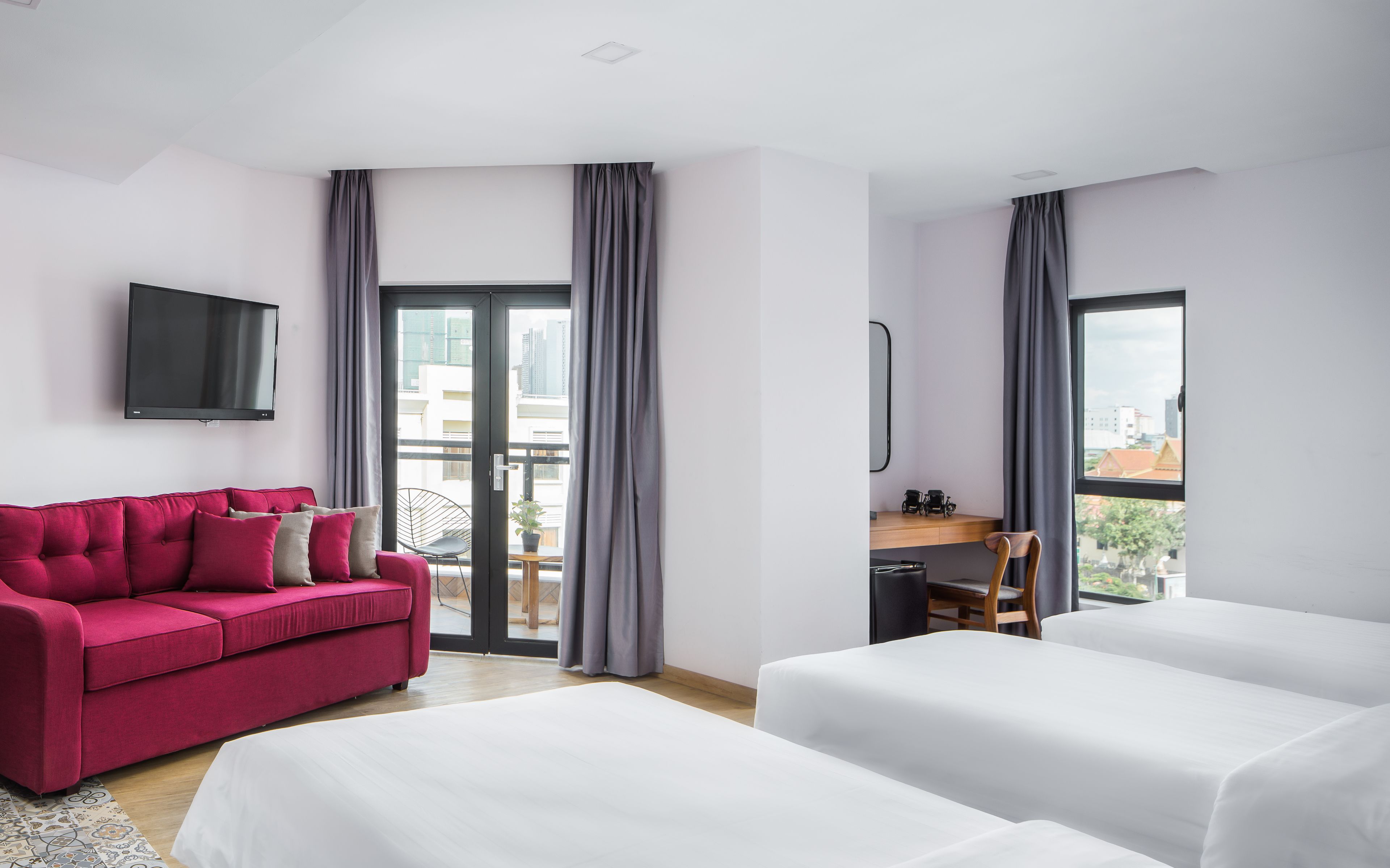 A hotel room with a red sofa, a white bed, a desk with a chair, and a TV mounted on the wall.