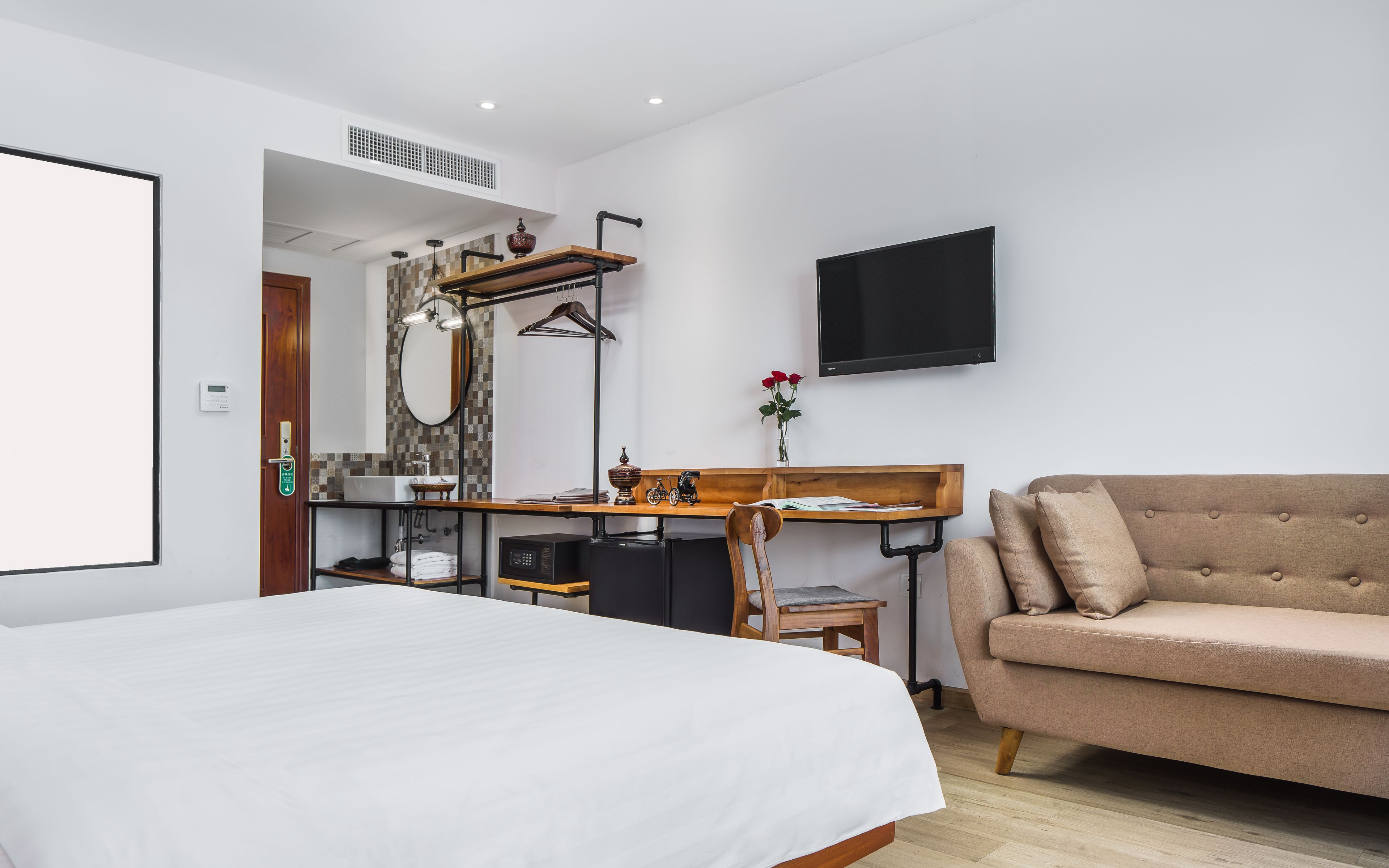 Un dormitorio con cama, escritorio, sillón, sofá, televisor y baño.
