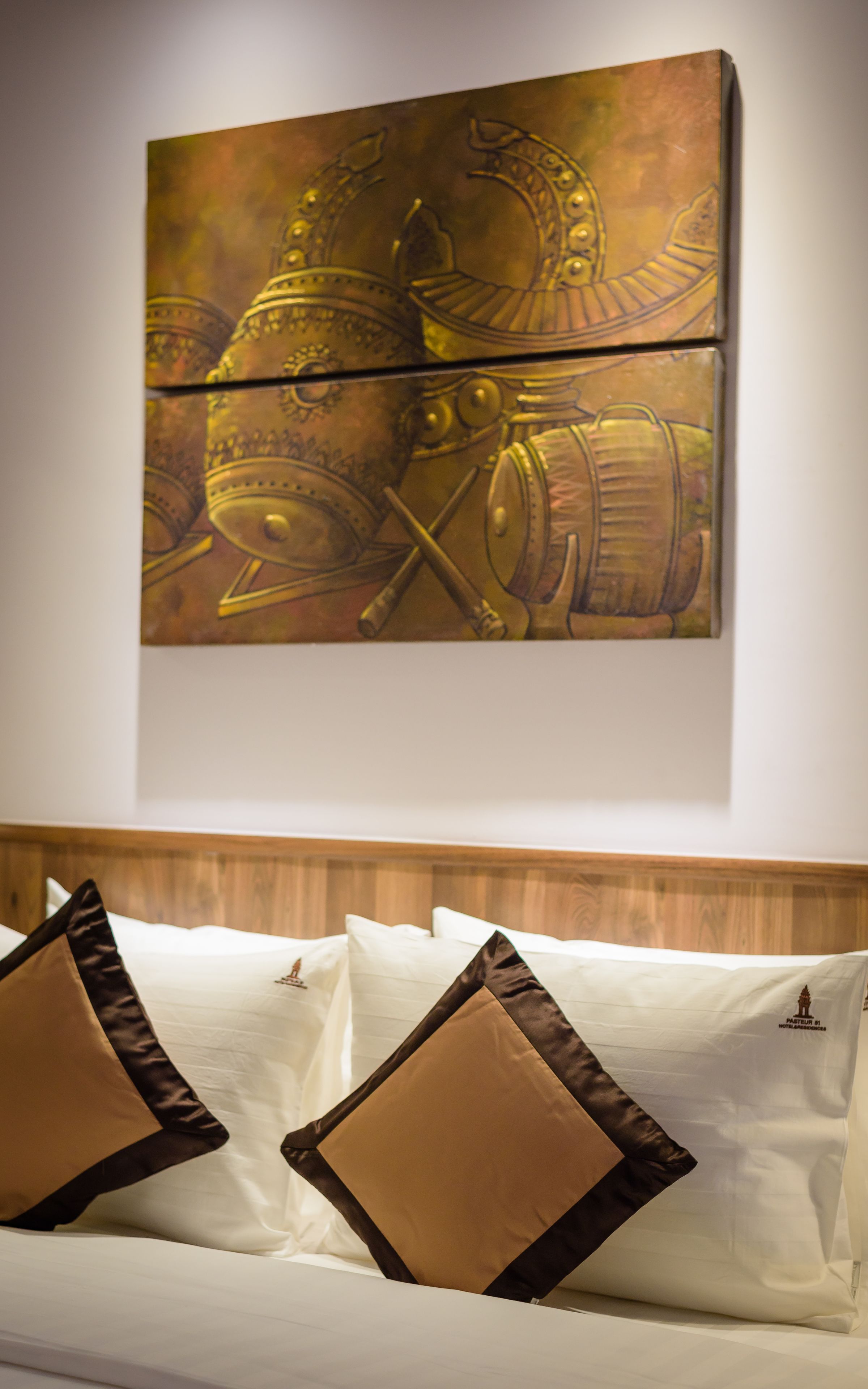 Un lit avec du linge de lit blanc et deux oreillers marron, un tableau représentant un instrument de musique en laiton accroché au mur, et une tête de lit en bois.