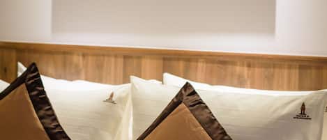 Un lit avec du linge de lit blanc et deux oreillers marron, un tableau représentant un instrument de musique en laiton accroché au mur, et une tête de lit en bois.