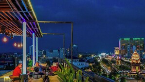 A rooftop terrace with a city view, tables, chairs, and a few people seated. - Phnom Penh 51 Hotel & Residences (Phnom Penh)