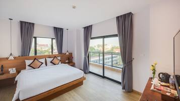 Una habitación de hotel moderna con una cama grande, un cabecero de madera, un escritorio con cafetera y vistas a la ciudad a través de amplios ventanales.