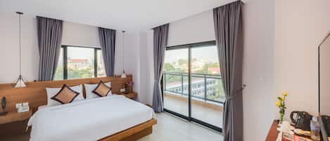 Una habitación de hotel moderna con una cama grande, un cabecero de madera, un escritorio con cafetera y vistas a la ciudad a través de amplios ventanales.