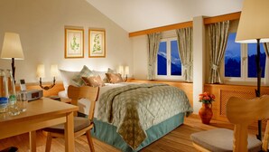 A hotel room with a bed, bedside lamps, a desk with a chair, a table, a vase with flowers, and a window with curtains. - Bürgenstock Hotels & Resort – Taverne 1879 (Ennetbuergen)