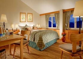 Habitación de hotel con cama, lámparas de noche, escritorio con silla, mesa, un florero con flores y una ventana con cortinas.