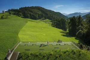Una cancha de tenis rodeada de colinas verdes exuberantes y un telón de fondo de montañas boscosas.