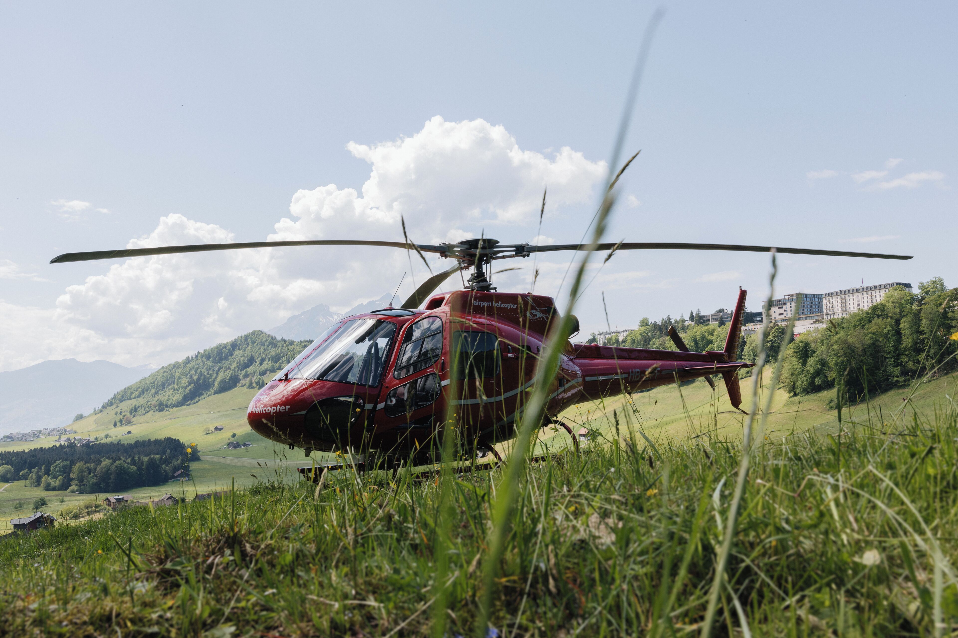 Un helicóptero rojo estacionado en un campo cubierto de hierba, con un paisaje montañoso al fondo.