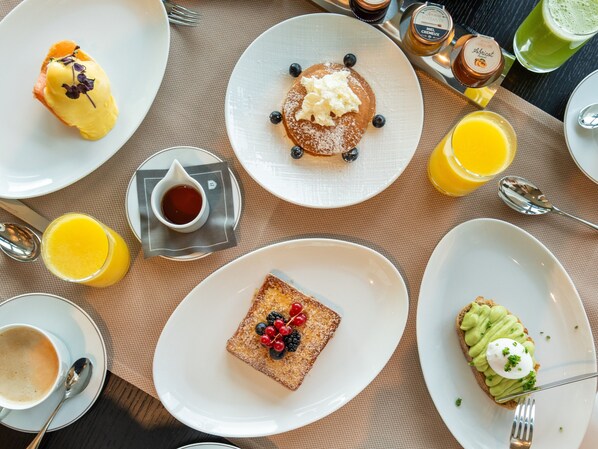 Un desayuno con diversas opciones, como panqueques, tostadas con frutos rojos y tostadas de aguacate, además de bebidas y salsas.