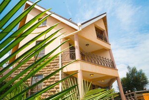 A multi-story building with a stone facade, balconies with metal railings, and a clear blue sky in the background.