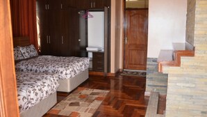 Un dormitorio con dos camas, un armario de madera, un baño con espejo y lavabo, y una escalera que sube a un piso superior.