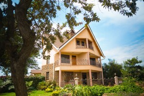 A two-story building with a balcony, surrounded by lush greenery and a clear sky. - Aloha Cottage (Ngong)