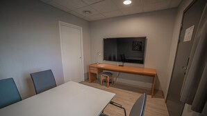 Una sala de conferencias con una mesa blanca, cuatro sillas, un escritorio de madera, una silla y un ventanal grande.