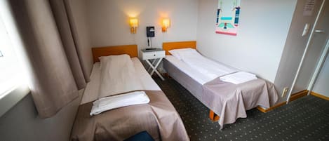 Habitación de hotel con dos camas individuales, una mesita, un teléfono y una obra de arte en la pared.