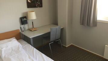 A hotel room with a bed, a desk, a chair, a telephone, a lamp, and a window with curtains.