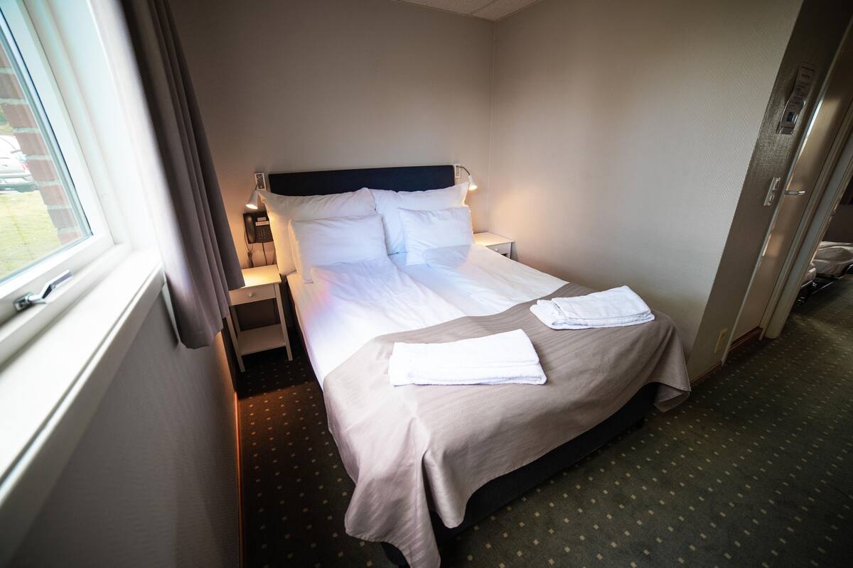 Une chambre d’hôtel avec un lit, une table de chevet, une lampe et une fenêtre.