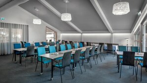 Un salón de conferencias con varias mesas y sillas, ventanas amplias y lámparas colgantes.