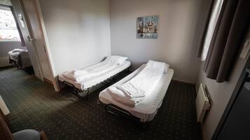 Habitación de hotel con dos camas individuales, una mesita, una silla y un radiador.