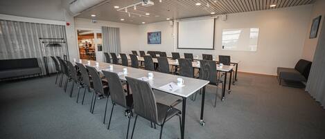 A conference room with a long table, chairs, a projector screen, and a whiteboard.