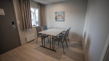 A room with a wooden floor, a white table with four chairs, a window with curtains, and a painting on the wall.