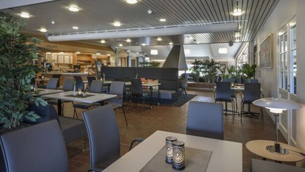 Un comedor moderno con mesas y sillas, un espacio de estar central y una cocina al fondo.