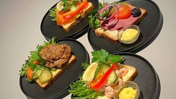 Four black plates with different food items, including sandwiches and shrimp, on a table.