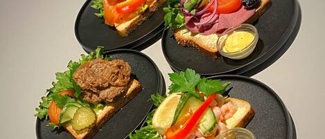 Cuatro platos negros con diferentes alimentos, como sándwiches y camarones, sobre una mesa.
