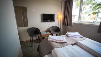 Una habitación de hotel con cama, dos sillas, escritorio, televisor y ventana con cortinas.