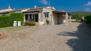 Une maison avec une allée en gravier, une terrasse dotée de mobilier d’extérieur et un mur en pierre.