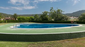 Une piscine dotée d’une plage verte, entourée de haies et d’arbres, et offrant une vue sur des collines en arrière-plan.