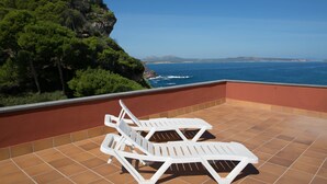 A terrace with two white lounge chairs and a view of the sea and a mountain. - 3 bedroom apartment in Aiguafreda, Begur. Terrace, panoramic views, pool. (Ref:H23) (Begur)