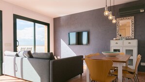 Een moderne woonkamer met een bank, eettafel, stoelen en een aan de muur bevestigde televisie.