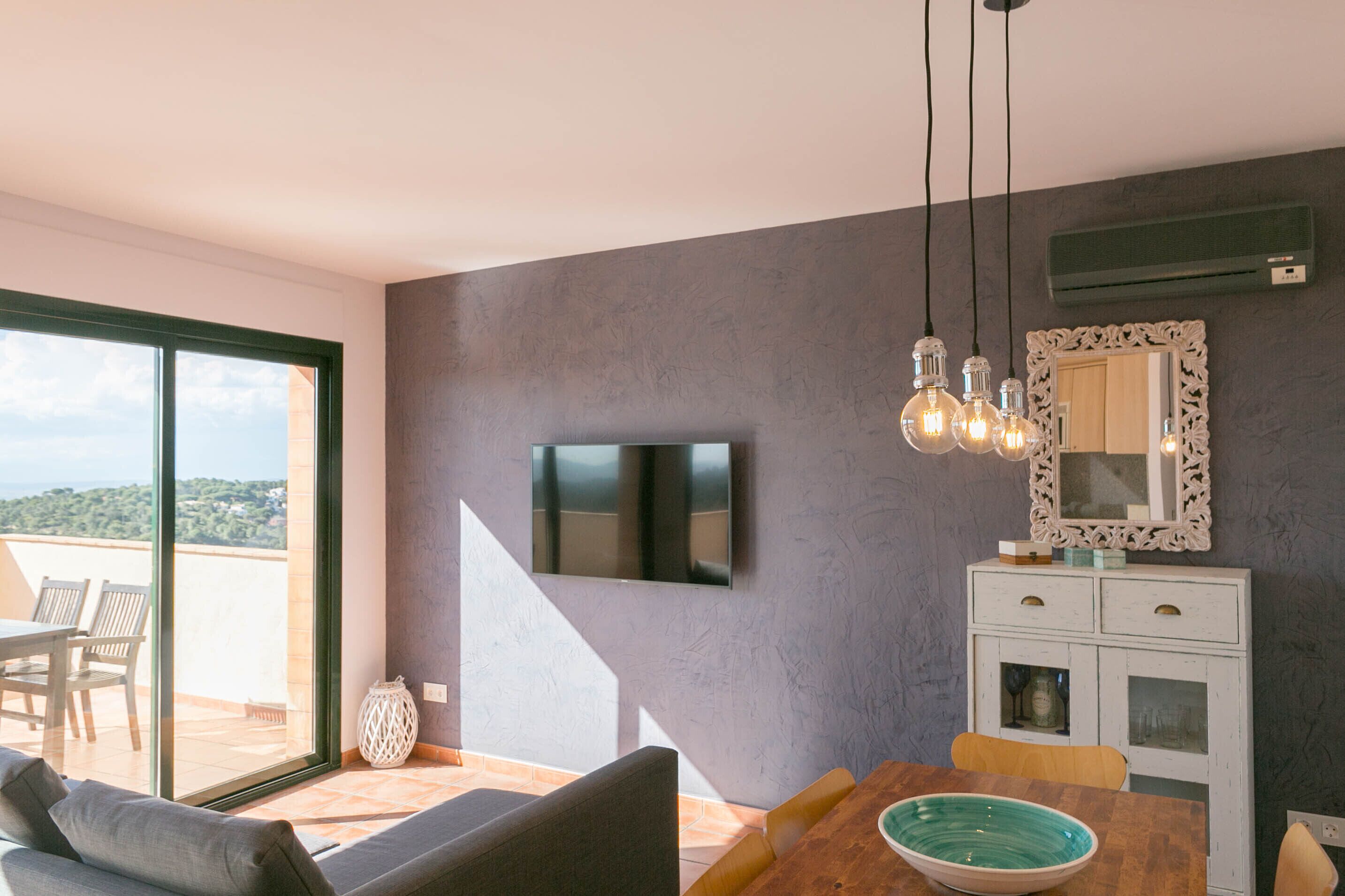 A modern living room with a flat-screen TV, a dining table with chairs, a sofa, and a decorative mirror.