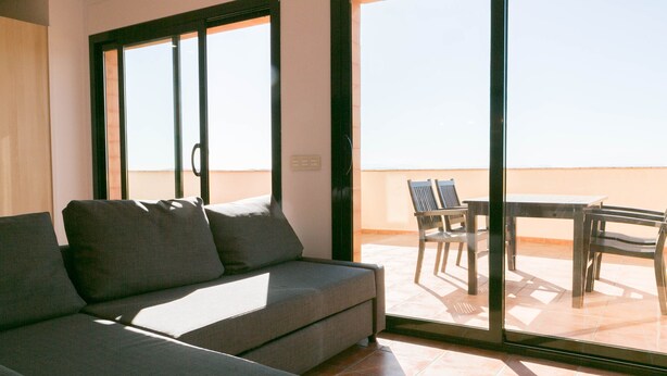 Een balkon met een bank en stoelen, grote ramen en uitzicht op de lucht.