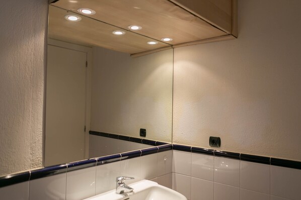 A bathroom with a white sink, a mirror, and a ceiling with recessed lighting.