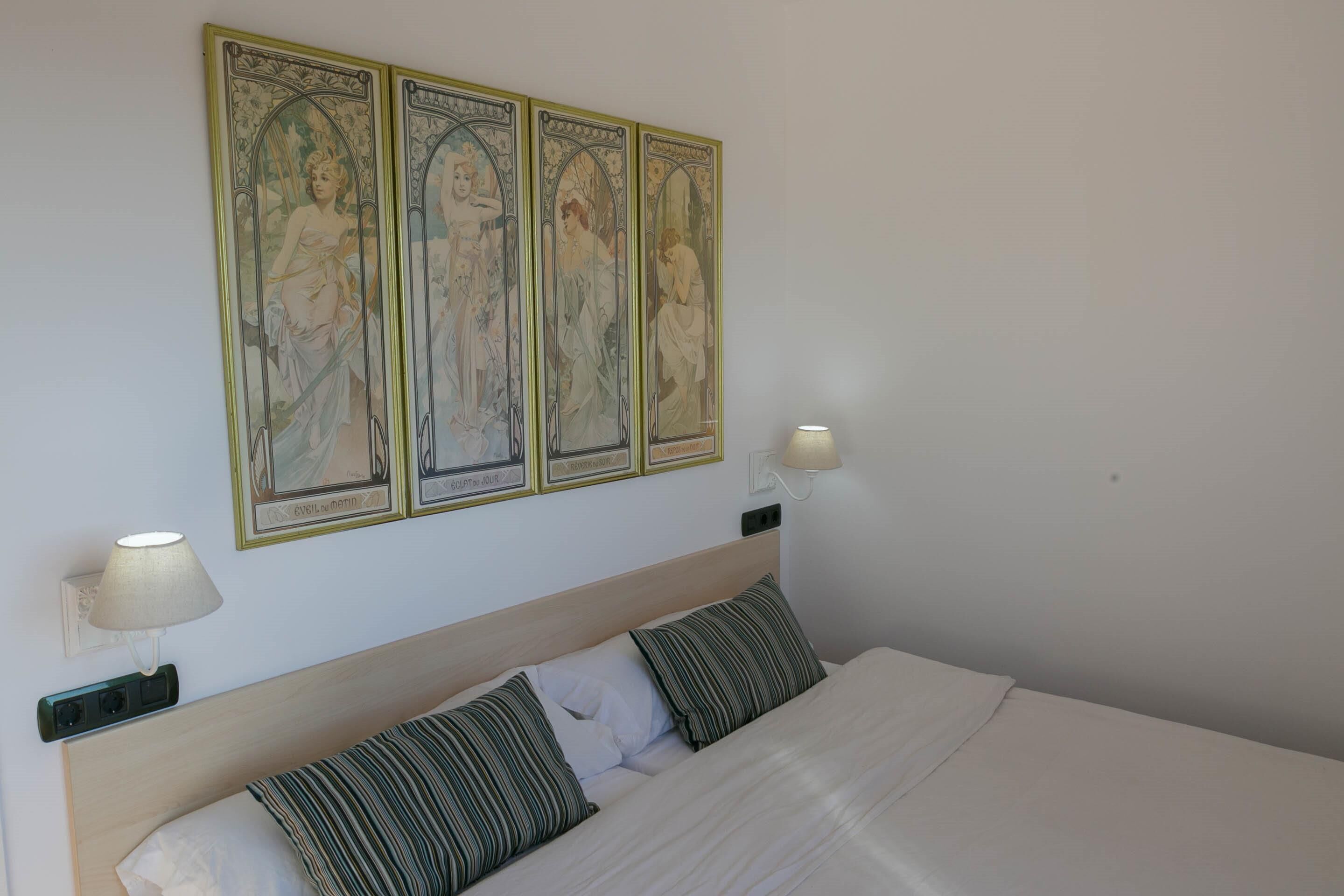 Een net opgemaakt bed met witte lakens en gestreepte kussens, een houten hoofdbord en een wandlamp.