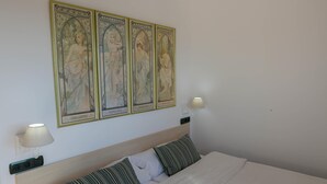 Een net opgemaakt bed met witte lakens en gestreepte kussens, een houten hoofdbord en een wandlamp.