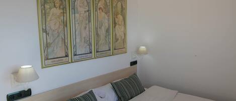 Een net opgemaakt bed met witte lakens en gestreepte kussens, een houten hoofdbord en een wandlamp.