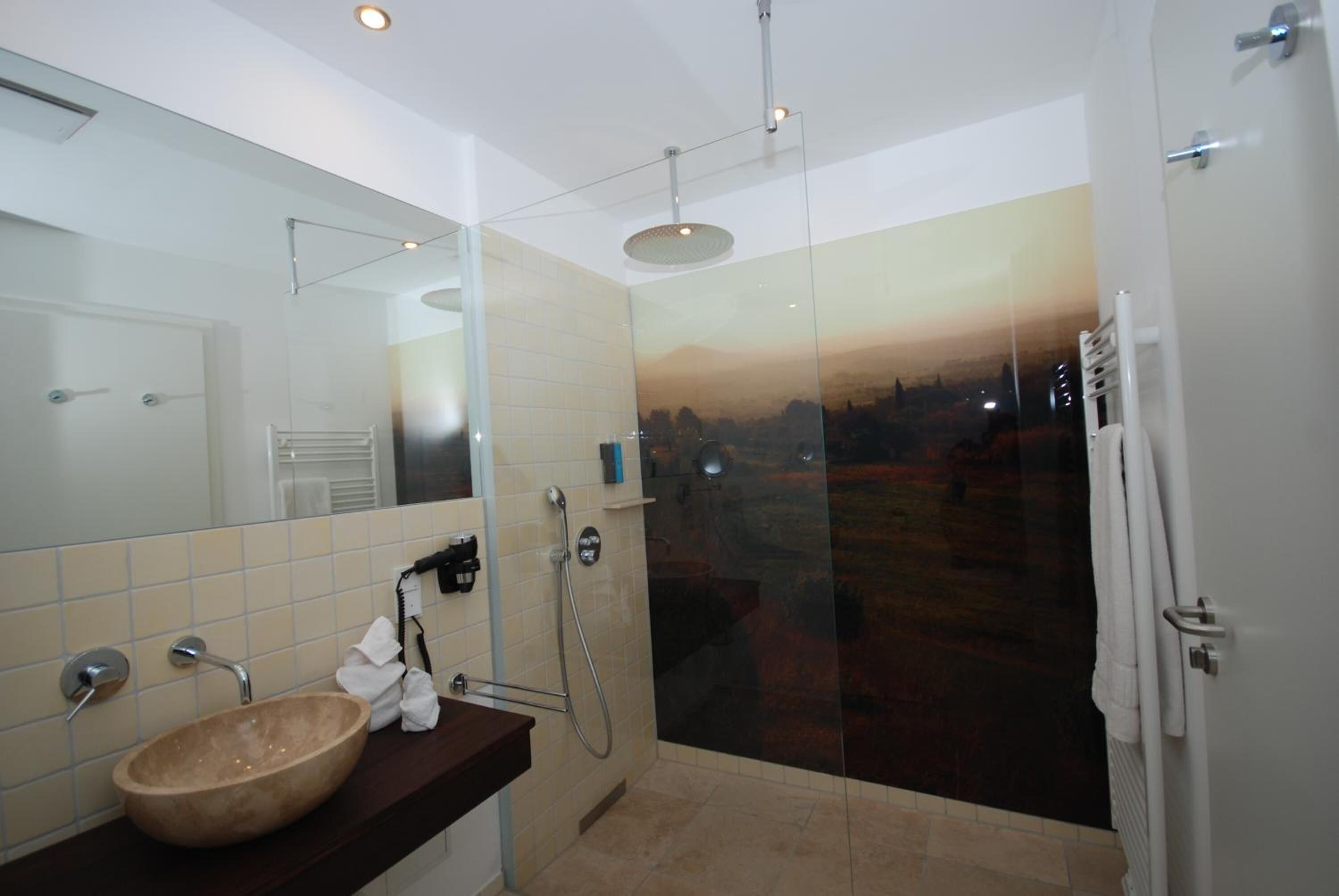 Ein modernes Badezimmer mit einer Glastrennwand zur Dusche, einem großen Spiegel und einem beige gefärbten Waschbecken.
